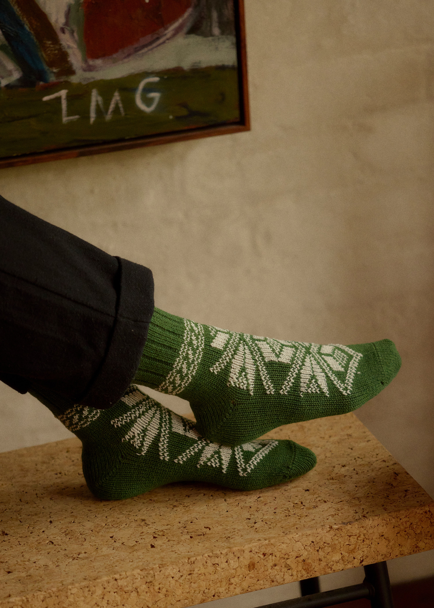 Green socks with white patterns worn by a person sitting on a wooden surface.